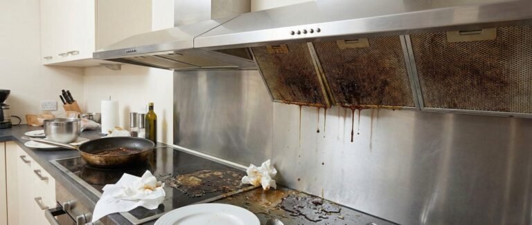 A single water droplet hanging from a modern kitchen range hood in focus.